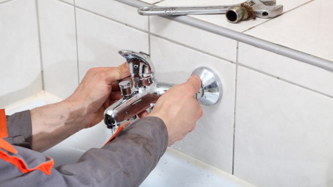 Plumber hands fixing water tap with spanner