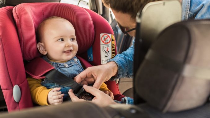 father strapping a child to child seat