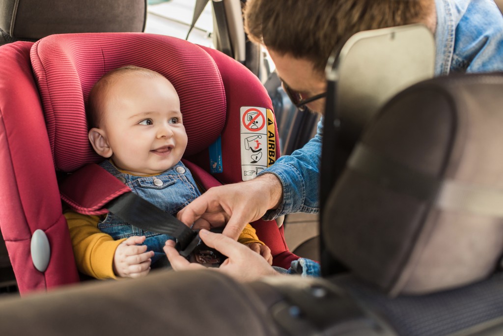 father strapping a child to child seat