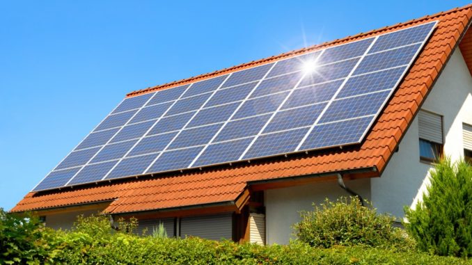 Solar panel on a red roof reflecting the sun and the cloudless blue sky