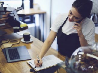 Woman writing on form while talking on the phone