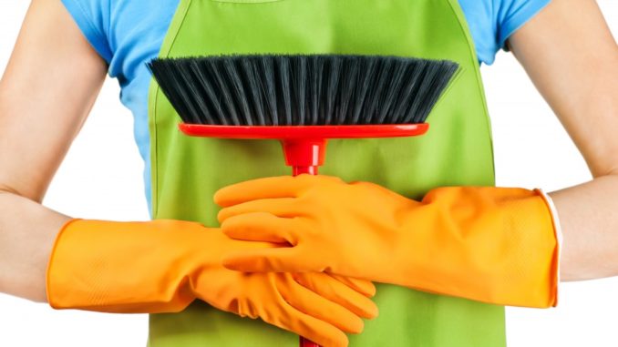 Woman wearing apron and gloves while holding a broom